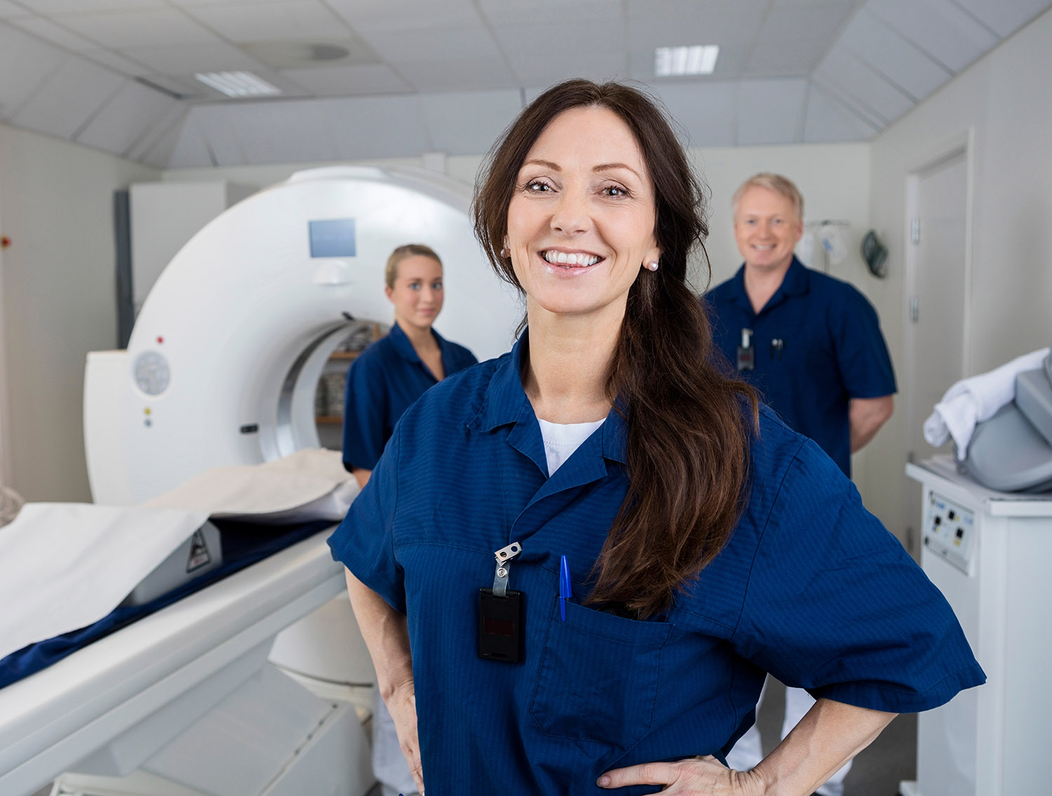 Portrait of happy female radiologist with colleagues standing by MRI machine in hospital Portrait of happy female radiologist with colleagues standing by MRI machine in hospital