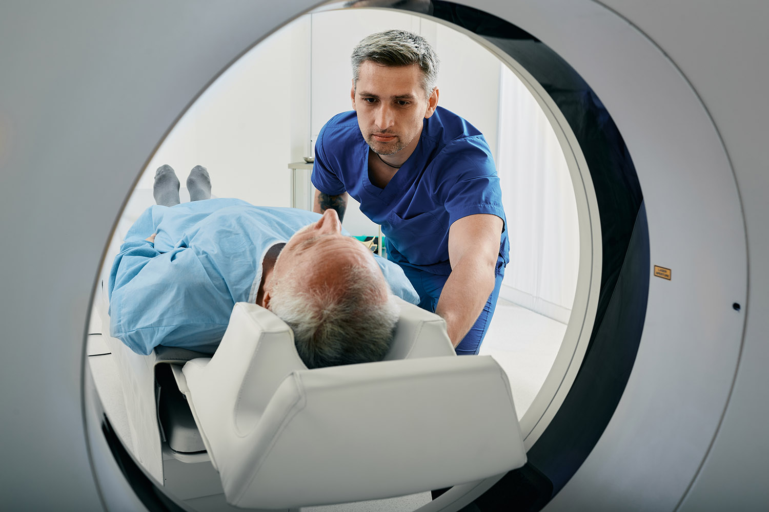 Senior man going into CT scanner. CT scan technologist overlooking patient in Computed Tomography scanner during preparation for procedure AdobeStock 528781828