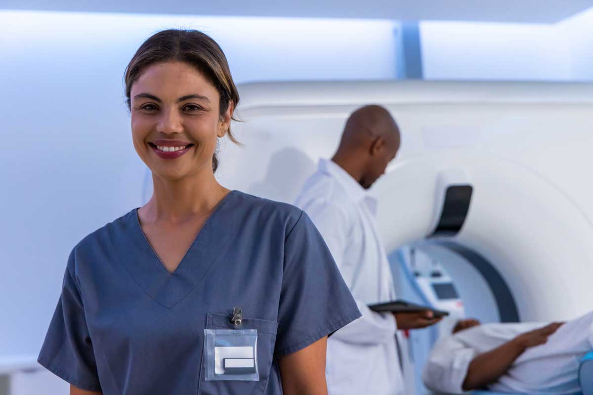 Smiling African American woman in gray scrubs showing badge, colleague using scanner in radiology Smiling African American woman in gray scrubs showing badge, colleague using scanner in radiology